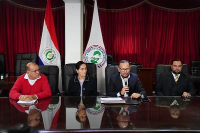 Pablo José Morinigo Cáceres, Walter Laguardia y Derlis León en mesa con banderas del IPS y Paraguay, expresiones tranquilas en ambiente formal.
