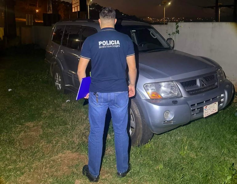 Hombre de policía de investigaciones de espaldas, junto a SUV gris, observando una escena urbana nocturna.