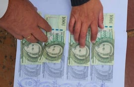Dos manos manipulan billetes de 100.000 guaraníes sobre papel, una lleva una alianza en el dedo anular.