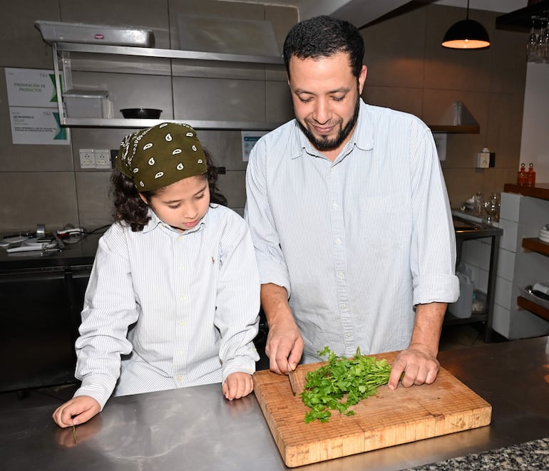 Luis Paredes. sonríe a su hija con banda verde mientras comparten un momento en la cocina en la celebración del Día del Padre.