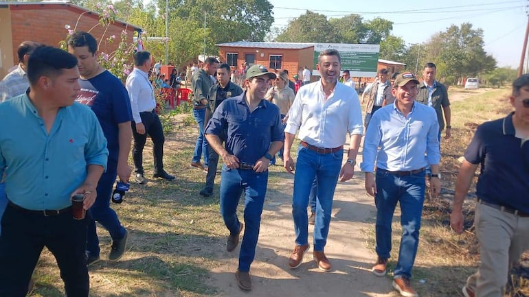 Pedro Alliana sonriente en camisa blanca, acompañado por Juan Carlos Baruja y otros hombres en un ambiente rural, durante un evento comunitario.