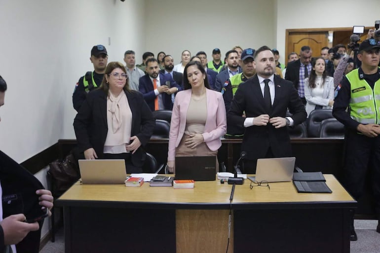 Yeimy Adle en blusa clara y abrigo negro, Verónica Valdez en traje rosa, y Silvio Corbeta en traje negro, en un salón de justicia.