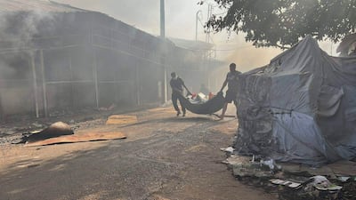 Dos hombres con ropa oscura cargan un bulto mientras el humo y las llamas envuelven un mercado en Itauguá.