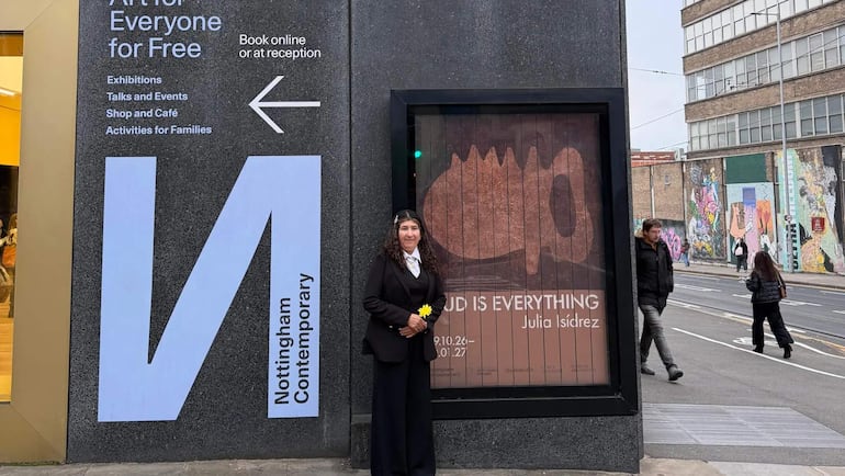 Julia Isídrez de pie frente a Nottingham Contemporary, vistiendo atuendo oscuro y sosteniendo una flor amarilla.