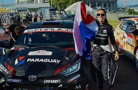 Andrea Lafarja sonríe con la bandera de Paraguay en sus manos, vestida con un uniforme de piloto, rodeada de un ambiente festivo.