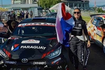 Andrea Lafarja sonríe con la bandera de Paraguay en sus manos, vestida con un uniforme de piloto, rodeada de un ambiente festivo.