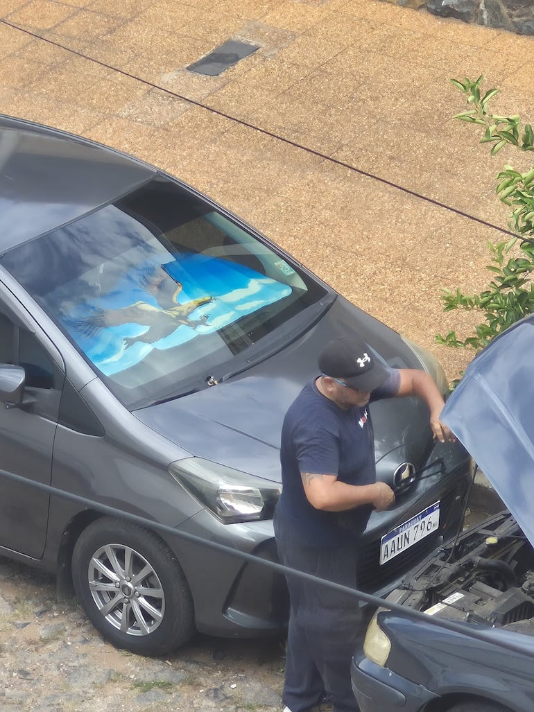 Momento en el que esta persona guarda el limpiaparabrisas utilizando el capó de su vehículo para no ser visto. 