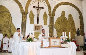 Sacerdote en vestimenta blanca dirige ceremonia, rodeado de niños con túnicas blancas y decoraciones religiosas en el altar.