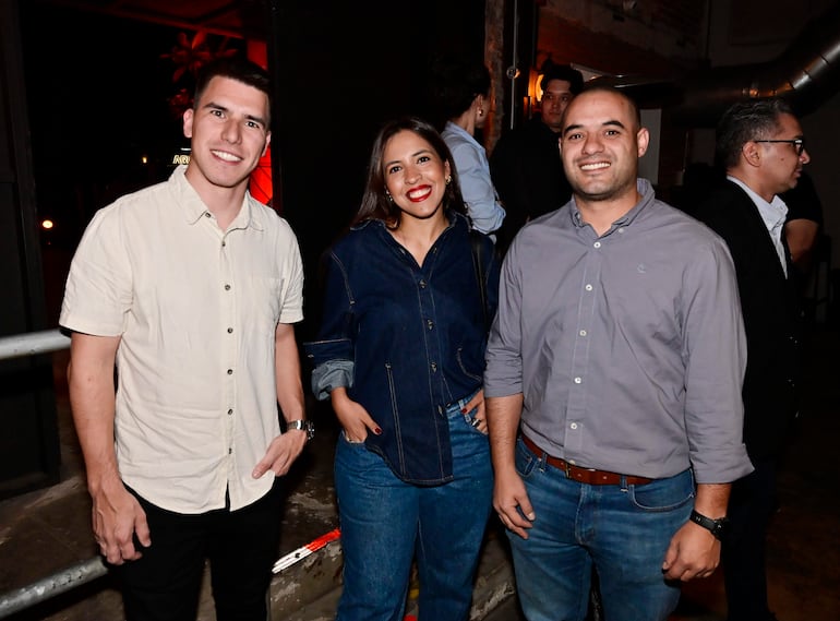 Hombre con camisa clara y pantalón oscuro, mujer con blusa de mezclilla, hombre con camisa gris; todos sonrientes en un ambiente social.