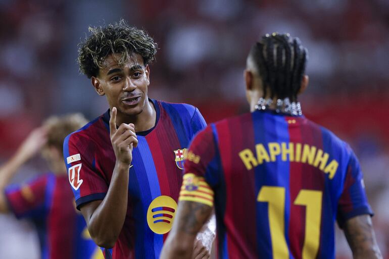 El delantero del Barcelona Raphinha (d) celebra con Lamine Yamal tras marcar el 1-3, durante el partido de LaLiga que Sevilla FC y FC Barcelona disputan este sábado en el estadio Ramón Sánchez-Pizjuán.