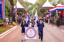 Estudiantes del Colegio Nacional Bernardino Caballero en trajes formales sosteniendo estandartes y banderas durante el desfile.