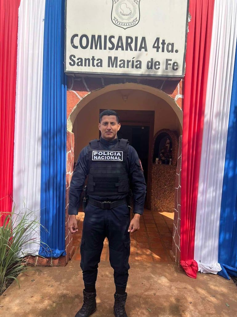 Brahian Barrios en uniforme negro de Policía Nacional, de pie frente a la Comisaría 4.ª decorada en colores nacionales.