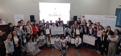 Grupo diverso de estudiantes sostiene cheques y diplomas, con expresión de alegría en un evento de premiación formal.