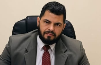 Cristhian Sánchez con traje oscuro y corbata, sentado en su oficina, mira a la cámara con expresión tranquila.