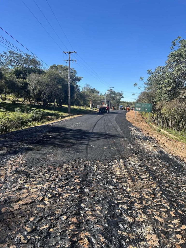 Carretera asfaltada en Cordillera, con trabajadores en acción y camión de suministros al fondo.