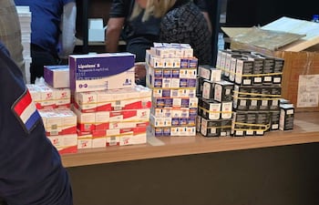 Mujer con uniforme y bandera observa cajas de medicamentos Lipoless sobre mesa de madera en un entorno comercial.