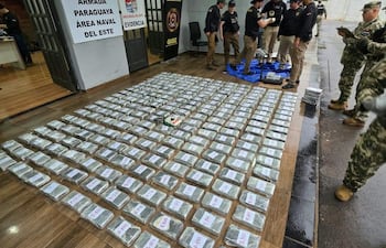 Seis agentes en uniforme táctico inspeccionan paquetes de droga sobre manta azul, con banner de la Armada Paraguaya al fondo.