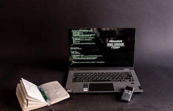 Ordenador portátil con código en pantalla oscuro, libreta y bolígrafo a un lado, sin personas presentes.