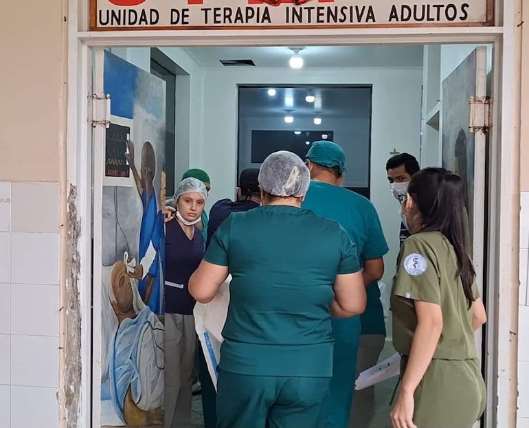 Varios profesionales de la salud, en scrubs verdes y azules, conversan en la entrada de la unidad de terapia intensiva, con un letrero visible.