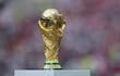 Trofeo dorado de la Copa Mundial sostenido por dos manos, con fondo difuso sugiriendo un ambiente festivo.