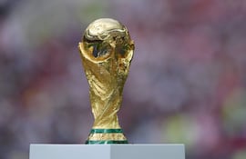 Trofeo dorado de la Copa Mundial sostenido por dos manos, con fondo difuso sugiriendo un ambiente festivo.