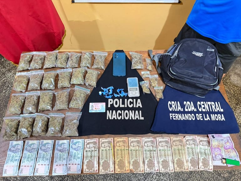 Mesa con bolsas de marihuana, billetes y chalecos de la Policía Nacional, sin personas visibles en la imagen.