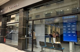 Dos mujeres de pie revisan sus teléfonos, mientras un hombre en chaleco marrón espera junto a la puerta de NORTE Cambios.