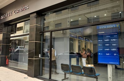 Dos mujeres de pie revisan sus teléfonos, mientras un hombre en chaleco marrón espera junto a la puerta de NORTE Cambios.