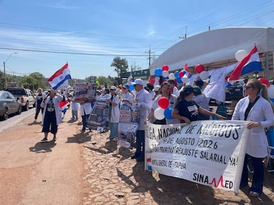Grupo de médicos en bata blanca sostiene pancartas en manifestación en Encarnación, con banderas de Paraguay ondeando al viento.