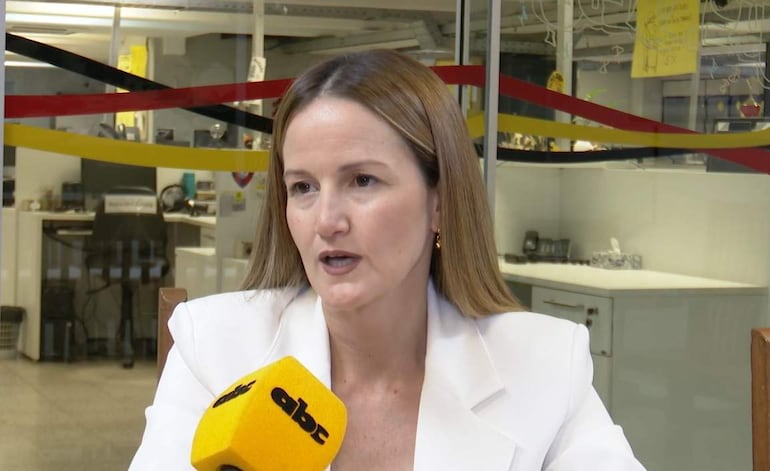 Soledad Núñez, mujer de cabello largo y lacio, viste un blazer blanco y sostiene un micrófono en un entorno de oficina.