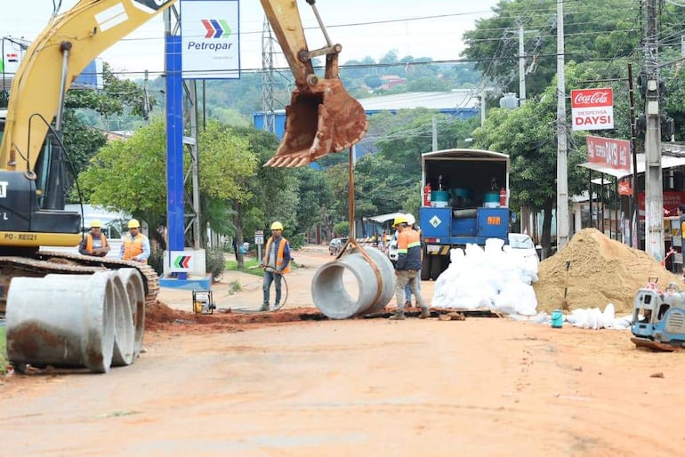 Cinco trabajadores con cascos amarillos y chalecos reflectantes, manipulando maquinaria en un ambiente de construcción con montones de tierra.