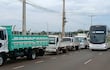 Camiones y autobús en el puente, con cielo nublado y postes de luz de fondo.