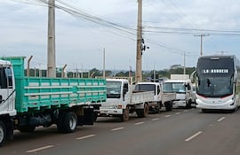 Camiones y autobús en el puente, con cielo nublado y postes de luz de fondo.
