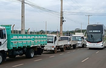 Camiones y autobús en el puente, con cielo nublado y postes de luz de fondo.