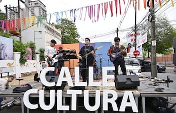 Cuatro músicos jóvenes en el escenario, dos con guitarras eléctricas, uno con un bajo, en un ambiente festivo con cintas de colores.