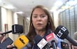 Celeste Amarilla, con chaqueta azul y aretes, habla en un podio rodeada de micrófonos de medios de comunicación.