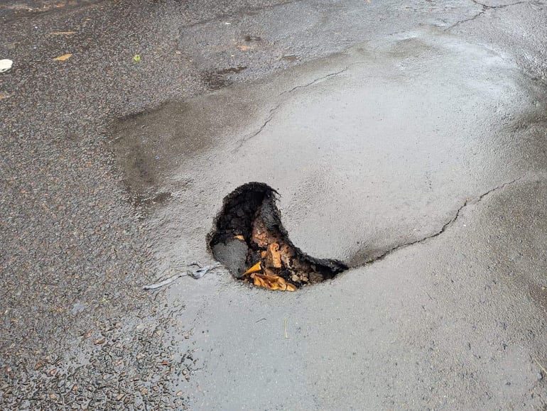Bache en calle pavimentada con agua estancada, rodeado de asfalto desgastado, sin personas presentes.