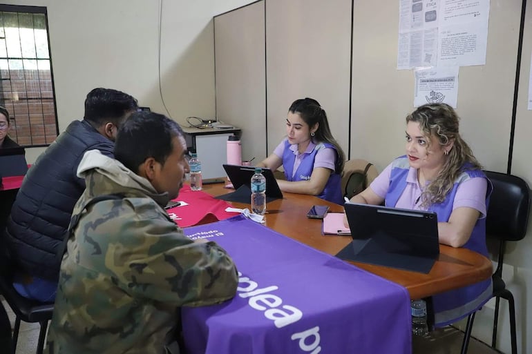 Tres personas sentadas en mesa, una mujer con gafas tomando notas y dos mujeres concentradas frente a tabletas. Ambiente de asesoría laboral.