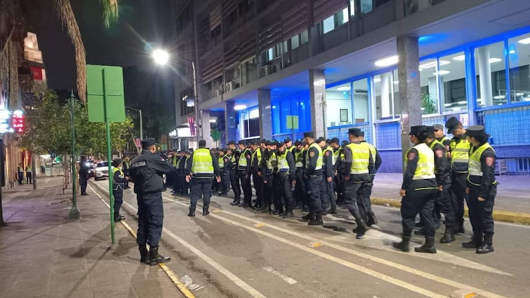 Grupo de policías en uniforme oscuro y chalecos amarillos alineados en una calle iluminada durante la noche.
