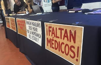 Grupo de hombres en reunión, con carteles que reclaman por falta de médicos y críticas a la inoperancia del estado.