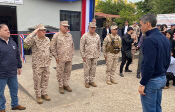Santiago Peña en abrigo oscuro observa a cuatro militares en uniforme de camuflaje alineados en atención.