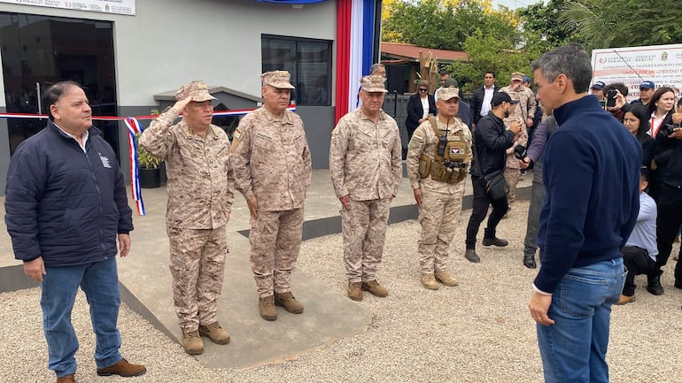 Santiago Peña en abrigo oscuro observa a cuatro militares en uniforme de camuflaje alineados en atención.