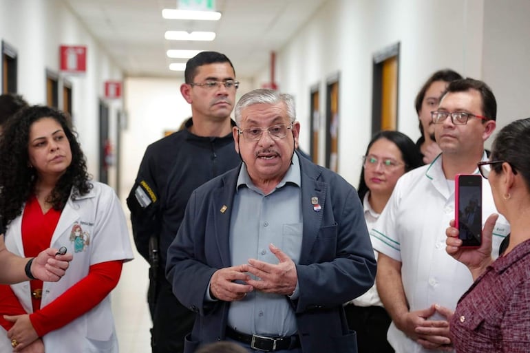 Isaías Ricardo Fretes, hombre canoso y con gafas, habla a un grupo de médicos en un pasillo con paredes blancas.