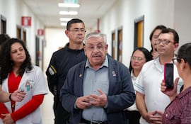 Isaías Ricardo Fretes, hombre canoso y con gafas, habla a un grupo de médicos en un pasillo con paredes blancas.