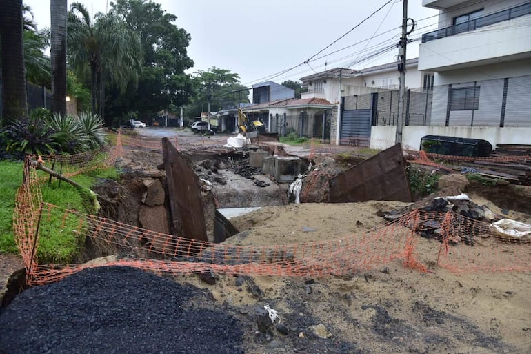 Calle desierta con excavaciones para obras de desagüe pluvial, cercas naranjas y edificios residenciales al fondo.