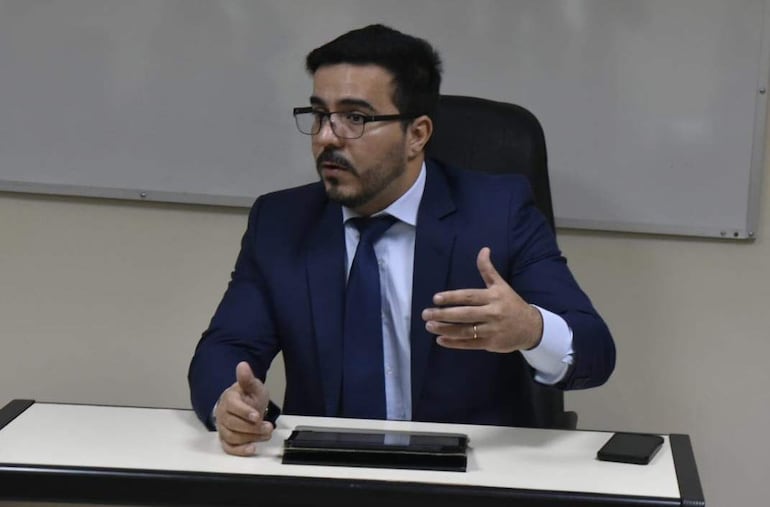 Rodrigo Estigarribia sentado en su oficina, con camisa blanca, traje oscuro y corbata, en una postura atenta y activa.