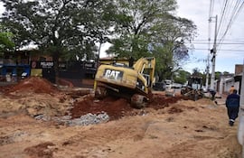 Excavadora CAT inclinada en obra, rodeada de tierra y piedras, con restaurantes al fondo y letrero de 'PELA DO Resto Bar'.
