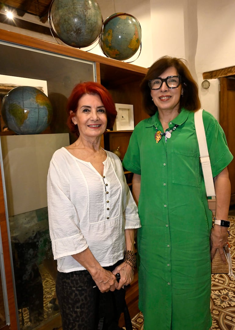 Dos mujeres sonrientes en galería: una con blusa blanca y pantalón animal, la otra con camisa verde y accesorios.
