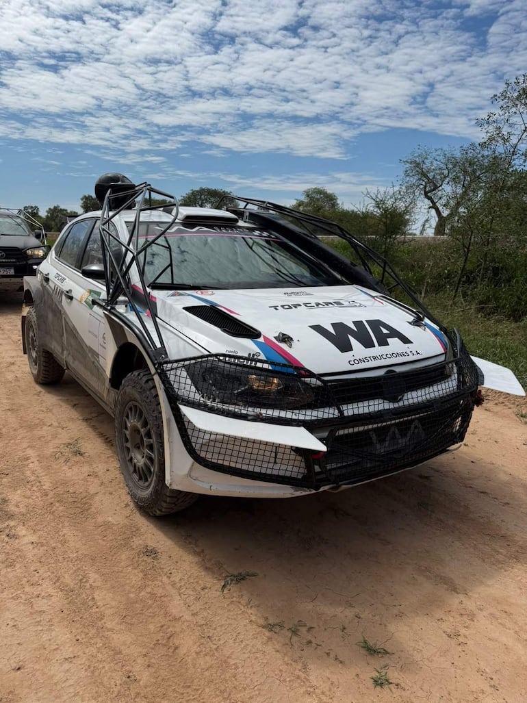 Coche de rally blanco con detalles en negro, preparado para competición en terreno arenoso, sin personas visibles.