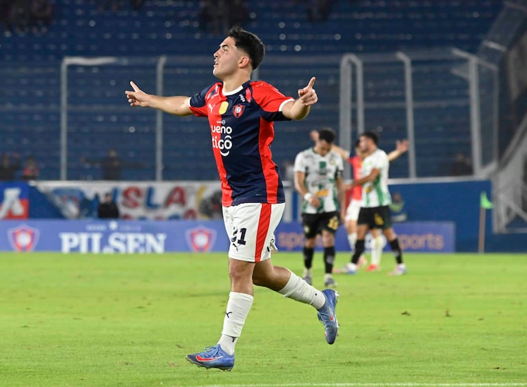 Jugador del Cerro Porteño con camiseta roja y azul levanta el brazo en celebración, mientras otros jugadores parecen desalentados en el fondo.